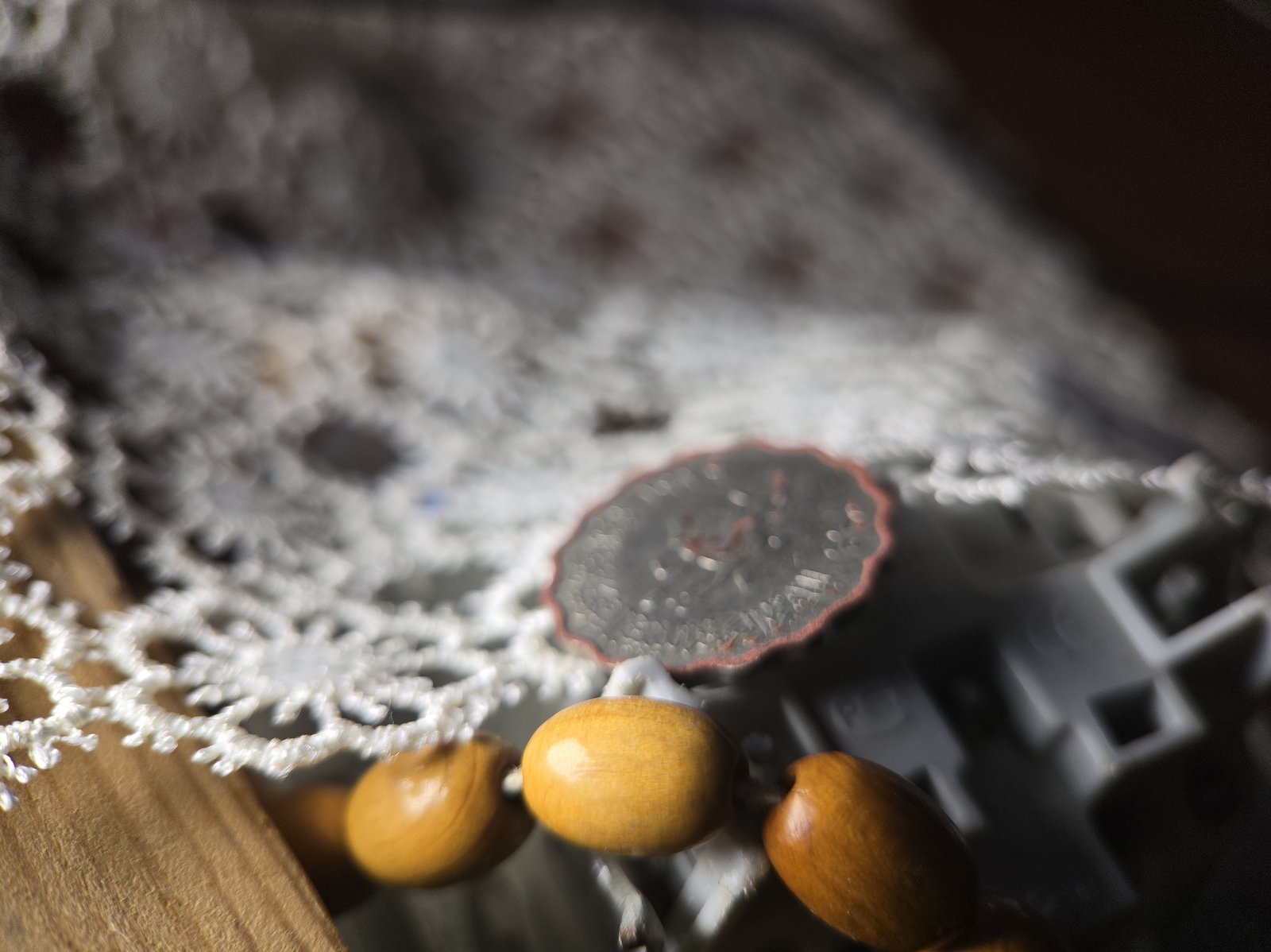 A single frame: only the wooden beads in front are sharp; the coin and the lace are blurred.