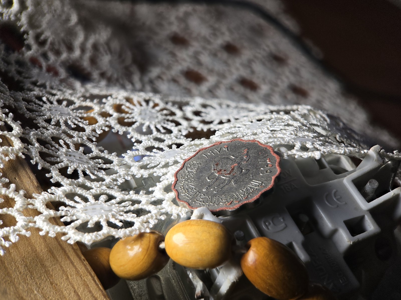 The stacked result: the wooden beads in front, the engraving on the coin and the lace behind it are all sharp.